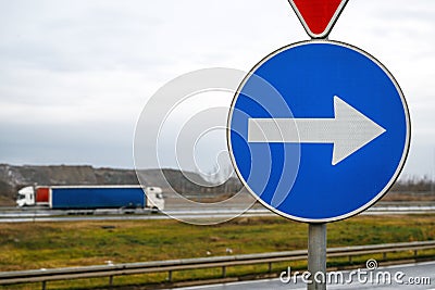 Mandatory direction arrow road sign on highway with two semi-trucks in background Stock Photo