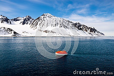 Maneuvering orange lifeboat in water in Arctic waters, Svalbard. Abandon ship drill. Lifeboat training. Man over board drill Stock Photo