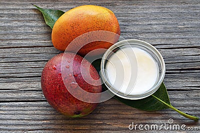 Mango body butter in a glass bowl and fresh ripe organic mango fruits on old wooden background.Spa,natural oils,organic cosmetic o Stock Photo