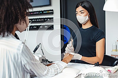 Manicure and pedicure salon, covid-19 concept. Asian girl in protective mask disinfects nails to client Stock Photo