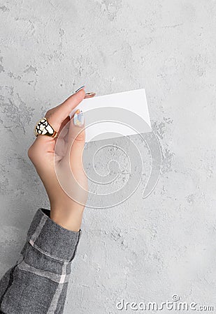 Manicured woman`s hand holding postcard on grey concrete background Stock Photo