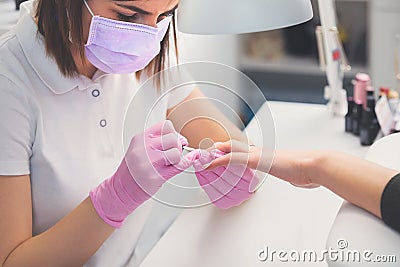 Manicurist in pink rubber gloves and medical mask applying nail polish to female nails Stock Photo