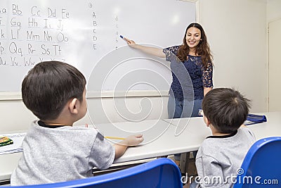 A female English teacher teaching two little boys, explaining ABC alphabet on board in classroom at school Editorial Stock Photo