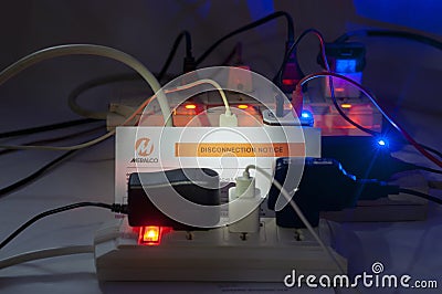 Low key night shot of multiple overloaded power boards extension socket with a MERALCO Di Editorial Stock Photo