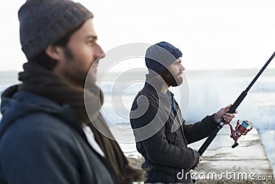 Manliness is at stake...who will catch the first fish. two young men fishing at the beach. Stock Photo