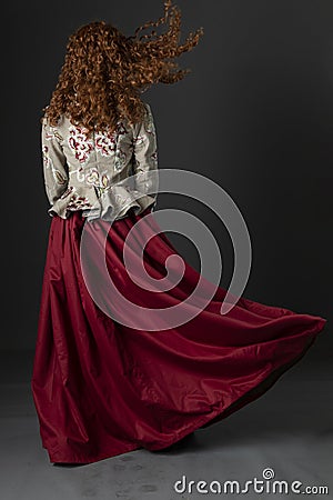 A mannequin with long curly red hair wearing a renaissance-style bodice and red skirt against a studio backdrop Stock Photo