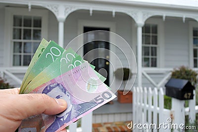 A mans hand holds NZ dollar bills against a front of North American hous Stock Photo