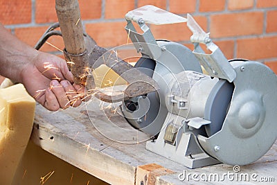 Mans hand sharpens a hoe on electric grindstone in rural shed Stock Photo