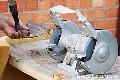 Mans hand sharpens a hoe on electric grindstone in rural shed Stock Photo