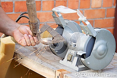 Mans hand sharpens a hoe on electric grindstone in rural shed Stock Photo