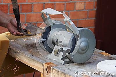 Mans hand sharpens a hoe on electric grindstone in rural shed Stock Photo