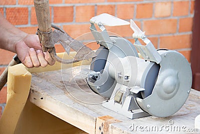 Mans hand sharpens a hoe on electric grindstone in rural shed Stock Photo