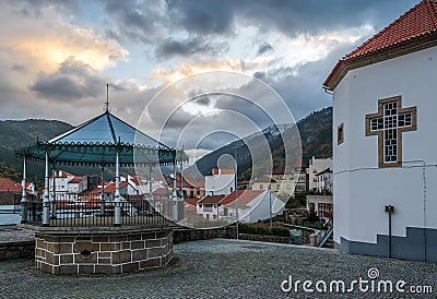 Manteigas village bandstand with houses and mountains in the background under dramatic sky, cross of StÂª Maria Mother Church Stock Photo