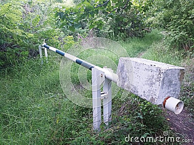 Manual barrier on forest track with stone blocking system. Exuberant vegetation environment. Manually operated level crossing Stock Photo