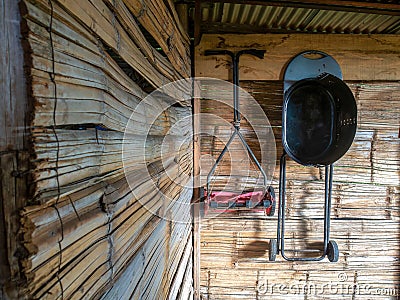 A manual lawn mower and a basic black grill hanging from a cane wall Stock Photo