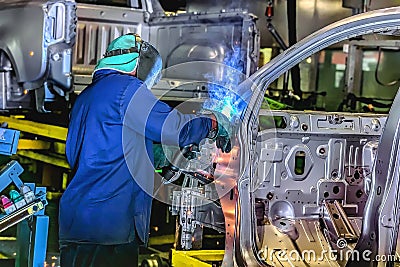 A welder busy welding on a motor vehicle production line. Safety gear is of high importance for safety. Stock Photo