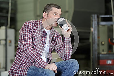 manual worker sitting on load cart while drinking coffee Stock Photo