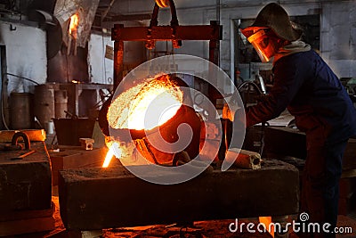 Industrial worker in protective gear pours molten metal at steel foundry. Manufacturing process in heavy industry with Stock Photo