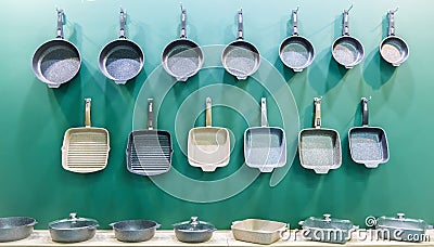 Many aluminum metal new modern cooking pans hang on the wall in the kitchen. Household goods, dishes, kitchen utensils. Storefront Stock Photo