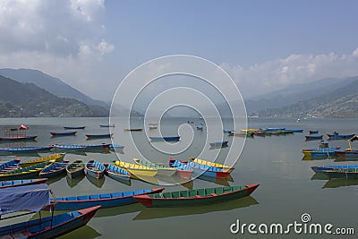 Many bright multicolored empty wooden boats on the Phewa lake on the background of a green mountain valley in the haze Stock Photo