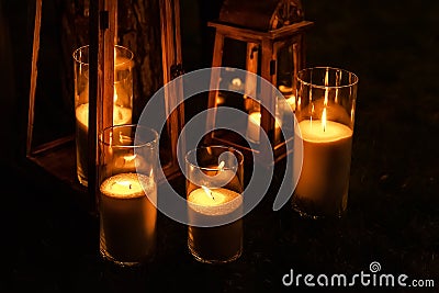 Many burning candles in glass and wooden lanterns on dark ground outdoor at night. Romantic party area. Diwali fire holiday Stock Photo