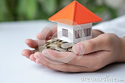 Many coins in the hand and a house with orange roofs placed on the hands The concept of buying and selling house, saving money for Stock Photo