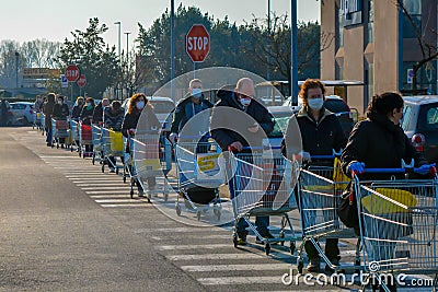 Many customers with masks waiting outside the grocery store before shopping, line of people with shopping carts in a parking lot Editorial Stock Photo