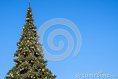 Many decorations and garland on a huge artificial Christmas tree outdoors on a blue sky background. At sunny summer day Stock Photo