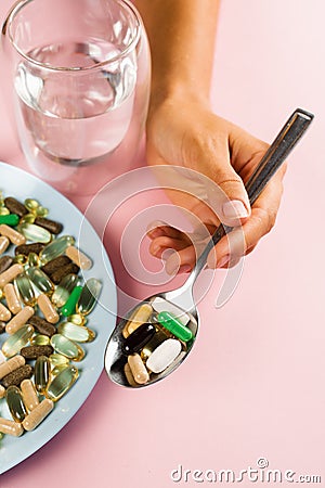 Many dietary supplements tablets, glass of water and spoon for daily pills intake on pink background. Set of mulvitamin Stock Photo