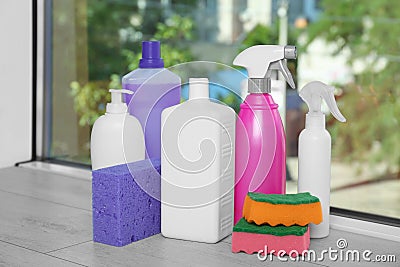 Many different bottles of detergents and sponges on window sill indoors. Cleaning supplies Stock Photo