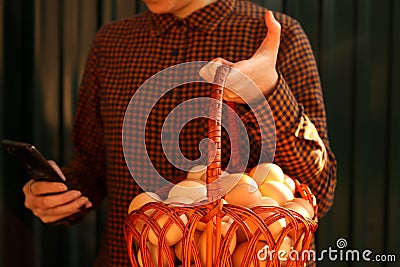 Many eggs in basket. Young woman holding whole basket of brown organic eggs on modern green background and scrolling Stock Photo