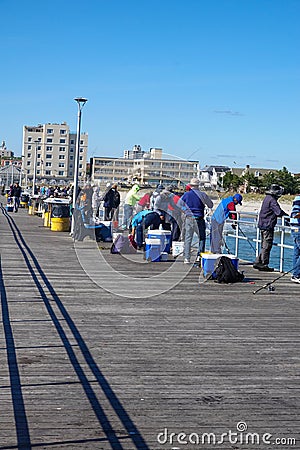 Many fisherman along the rail fence on one side of a long pier fishing in the ocean Editorial Stock Photo