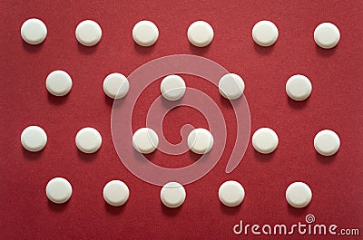 Many generic small round white pills, lots of little tablets on red background close up. Simple group of little pills, medicine Stock Photo
