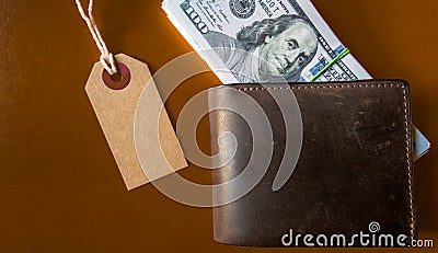 Many hundreds of dollars banknotes in a leather wallet with a brown tag, price tag on a brown background. Flat lay. Background, Stock Photo