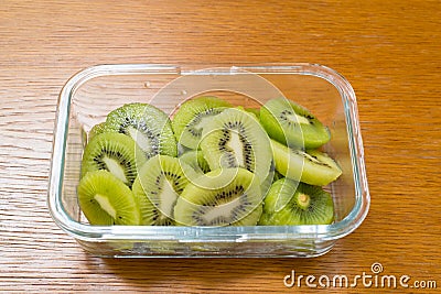 Many kiwi slices in a glass crisper on a wooden table. Kiwifruit slices without peel Stock Photo