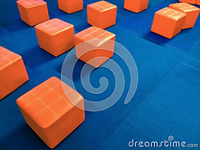 Many orange cubic padded stool chairs on blue carpet in event stage area inside of shopping mall Stock Photo