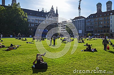 Many people relax on the grass and enjoying the sun on a green lawn at the Marienhof in the inner city of Munich Editorial Stock Photo