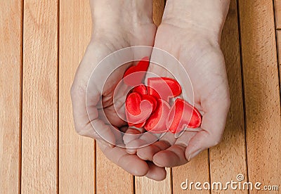 Many red hearts in women palms. Wooden background Stock Photo