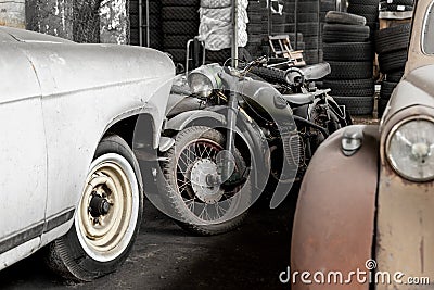 Many rusty abandoned forgotten antique oldtimer old car and motorcycles at junkyard factory storage warehouse indoors Editorial Stock Photo