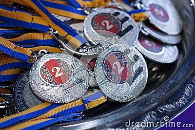 Many silver medals with blue ribbons on a silver tray, awards of champions, sport achievements, second place, prize for the winner Stock Photo