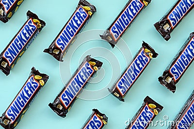 Many Snickers chocolate bars lies on pastel blue paper. Snickers bars are produced by Mars Incorporated. Snickers was created by Editorial Stock Photo