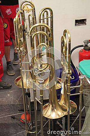 Many trombones stand around on their trombone stands in the aisle. Imperial College London big band rehearsal room. Brass Stock Photo