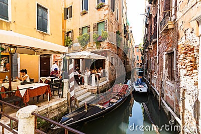 Many visitors in typical tiny cafe in Venice near canal with gondolas and boats Editorial Stock Photo