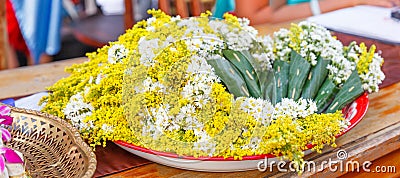 Many white chamomile flowers and yellow acacia flowers bouquets wrapped in cones, made by folded banana leaves, are prepared for Stock Photo