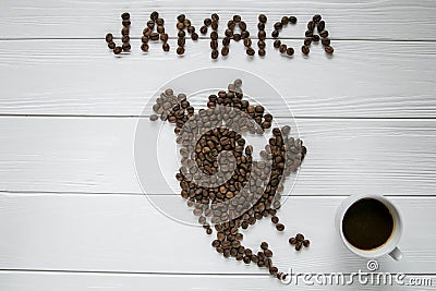 Map of the Jamaica made of roasted coffee beans laying on white wooden textured background with cup of coffee Stock Photo