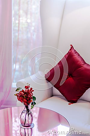 Nice flower in glass bottle on round table with armchair and pillow in background Editorial Stock Photo