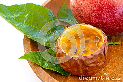 Maracuja cut in half and whole in small glass container peel of the fruit with wooden spoon and leaf on plate and white background Stock Photo