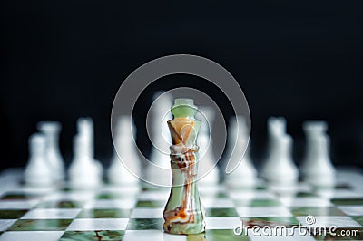 Marble chess board from white and green marble. Black chess king on chessboard against white chess pieces. Concept one against all Stock Photo