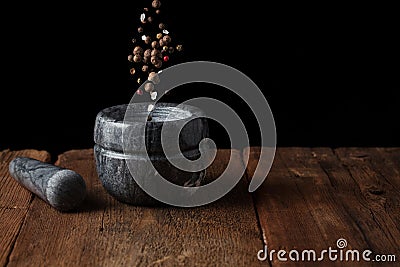 Marble mortar on old wooden table on black background with copy space. Pepper seeds fall into the mortar. freezer food Stock Photo