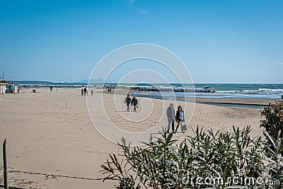 Couples stroll along the beac in Nettuno, Italy on a hazy, sunny day Editorial Stock Photo